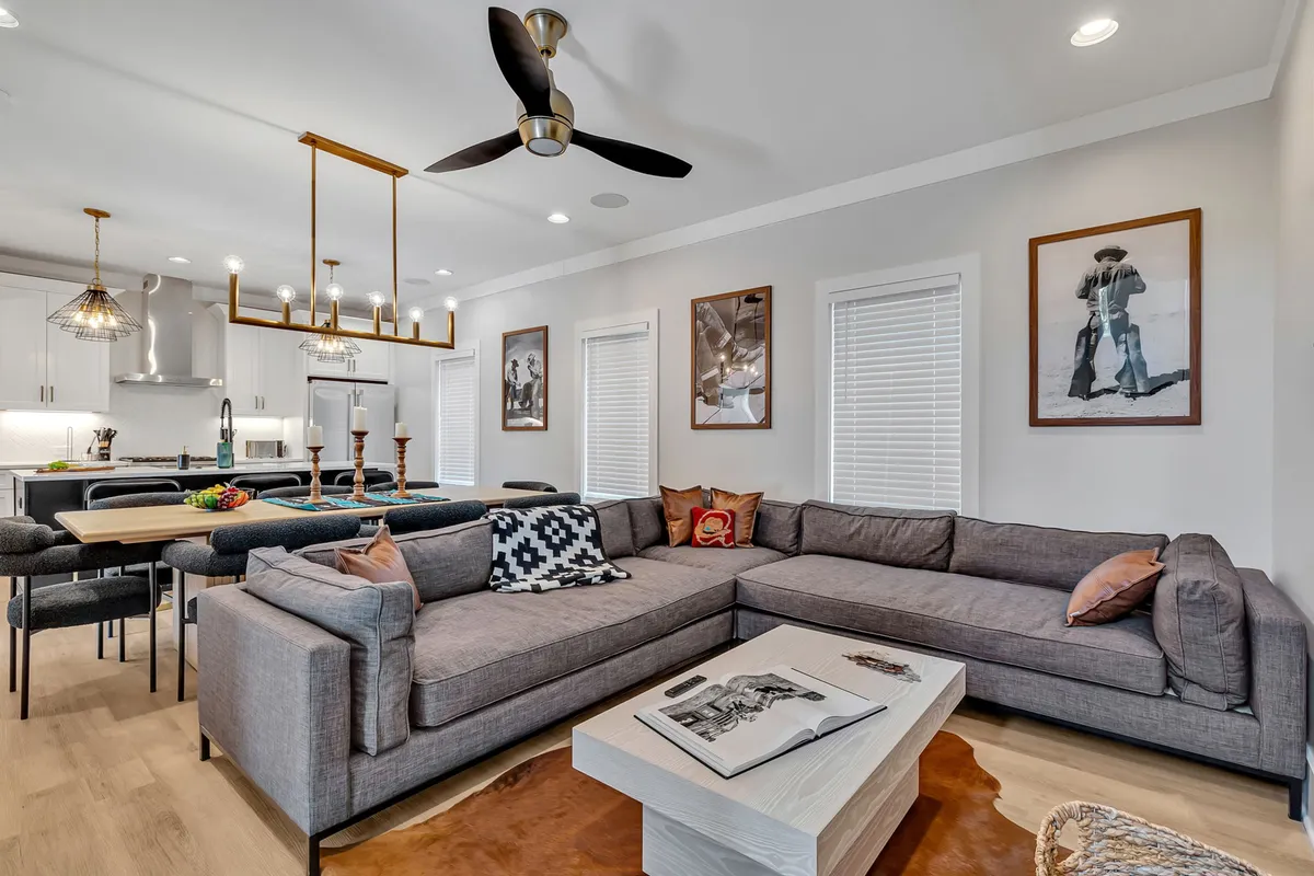 This image highlights a large sectional sofa facing a stylish coffee table, with a dining table under a hanging light fixture visible in the background. Artwork adorns the walls, and the overall decor is both inviting and sophisticated. The open layout allows for easy movement and visual connection between the living and dining areas.