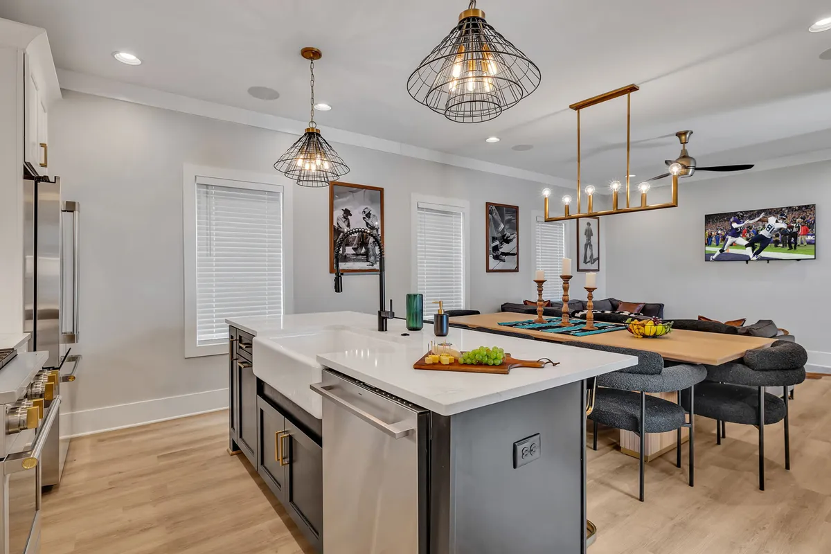 A seamless view of the kitchen island in the foreground, transitioning into a stylish dining table and wall art beyond. The lighting fixtures are modern and welcoming, and the overall ambiance is bright and sociable—perfect for hosting meals or casual brunches.