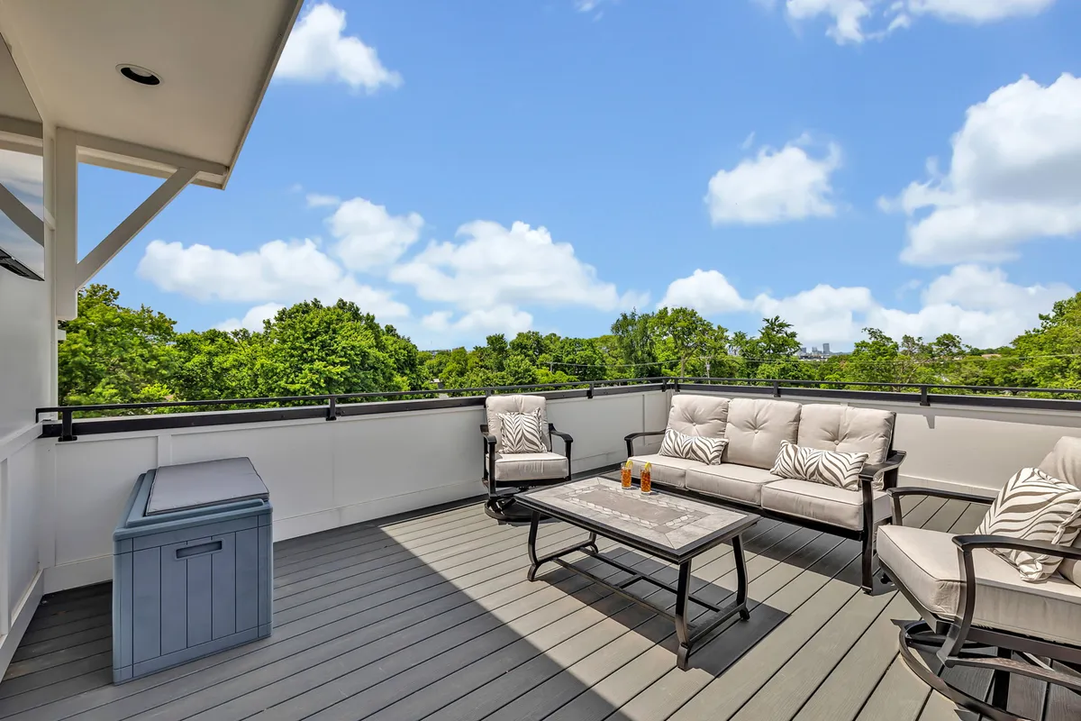 A tranquil outdoor lounge area showcases comfortable seating and a coffee table, surrounded by lush greenery and an open sky, suggesting the elevated feel of a rooftop deck. The environment is perfect for sunset cocktails, intimate gatherings, or relaxed stargazing.