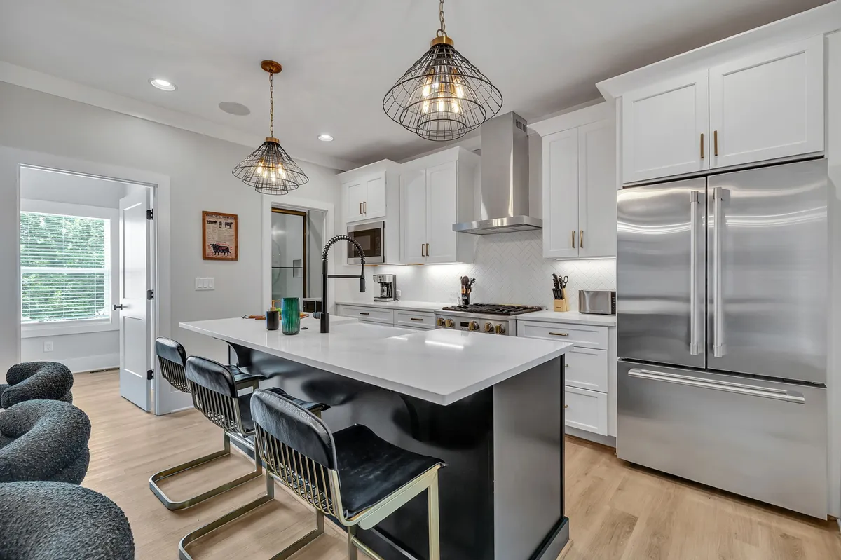The modern kitchen is anchored by a generous island with bar stools, pendant lighting overhead, and sleek stainless steel appliances. The space is thoughtfully arranged for both socializing and culinary pursuits, with ample seating at the island encouraging casual conversation.