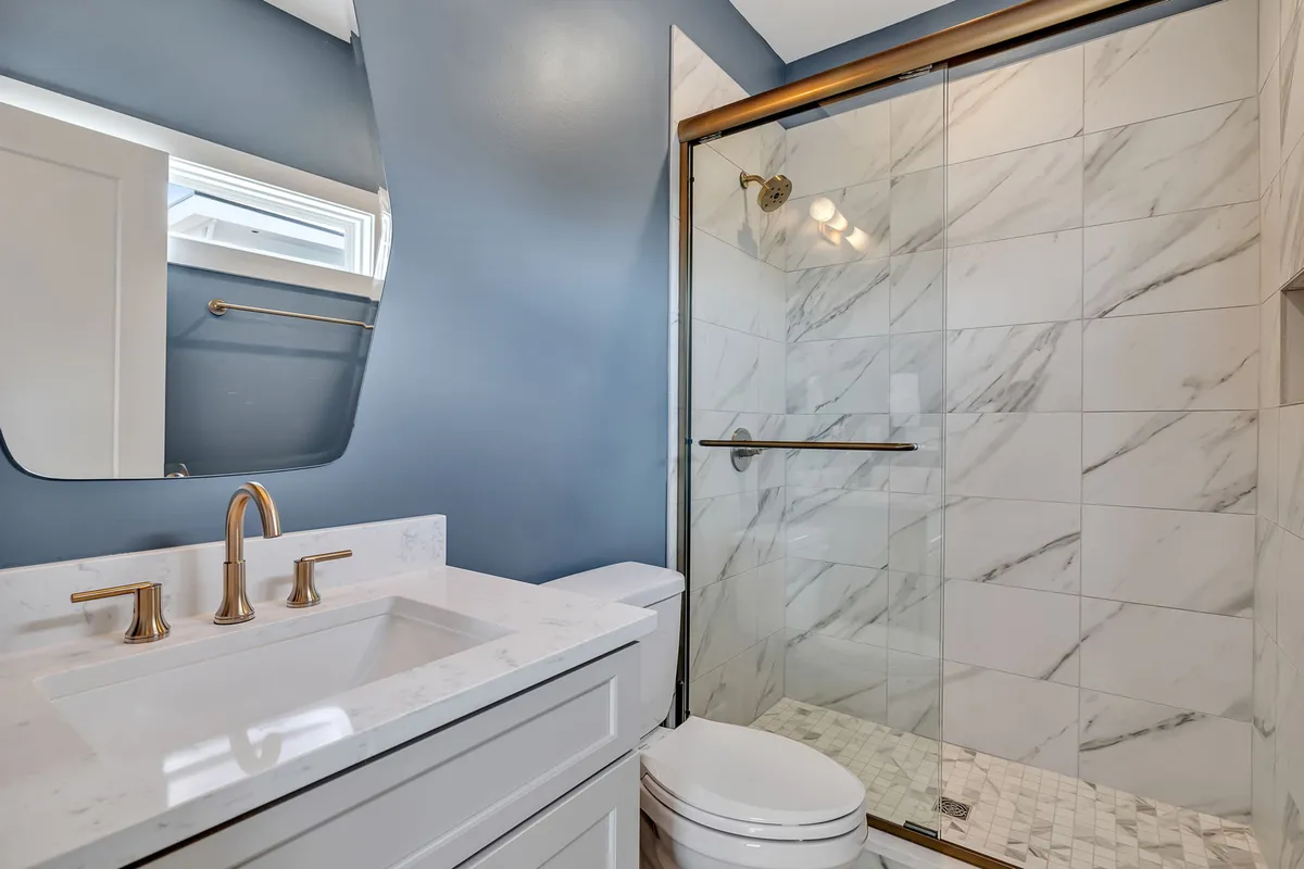A luxurious, spa-inspired bathroom featuring a marble shower, brushed gold fixtures, and a white vanity. The space is bright, upscale, and designed for relaxation and self-care routines.