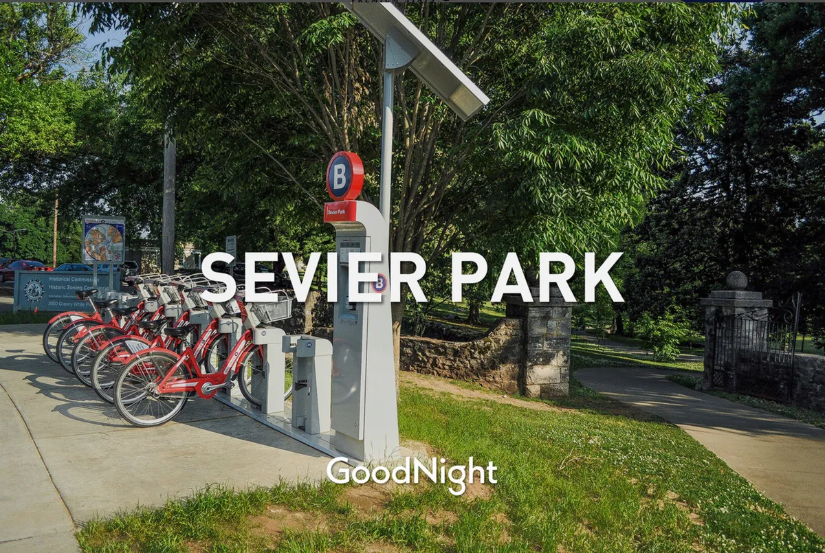 A vibrant park entrance scene featuring a bicycle rental station, park signage, and a leafy, welcoming pathway inviting exploration and outdoor activities. The active, community-oriented setting is ideal for family play and relaxation.