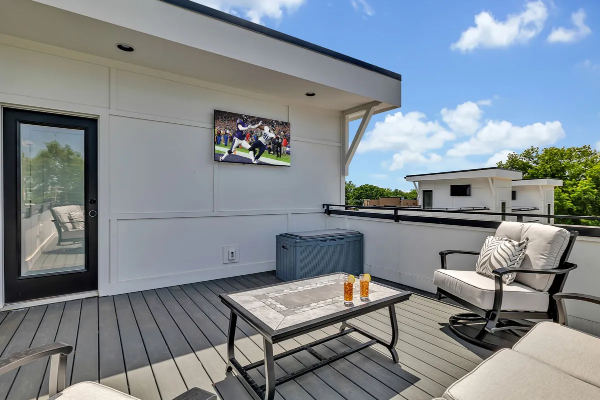 An outdoor rooftop seating area with comfortable couches, a coffee table, and a large television screen. The scene is designed for socializing, relaxing, and entertainment, set against an open sky, suggesting a private and elevated space to unwind after exploring the city.